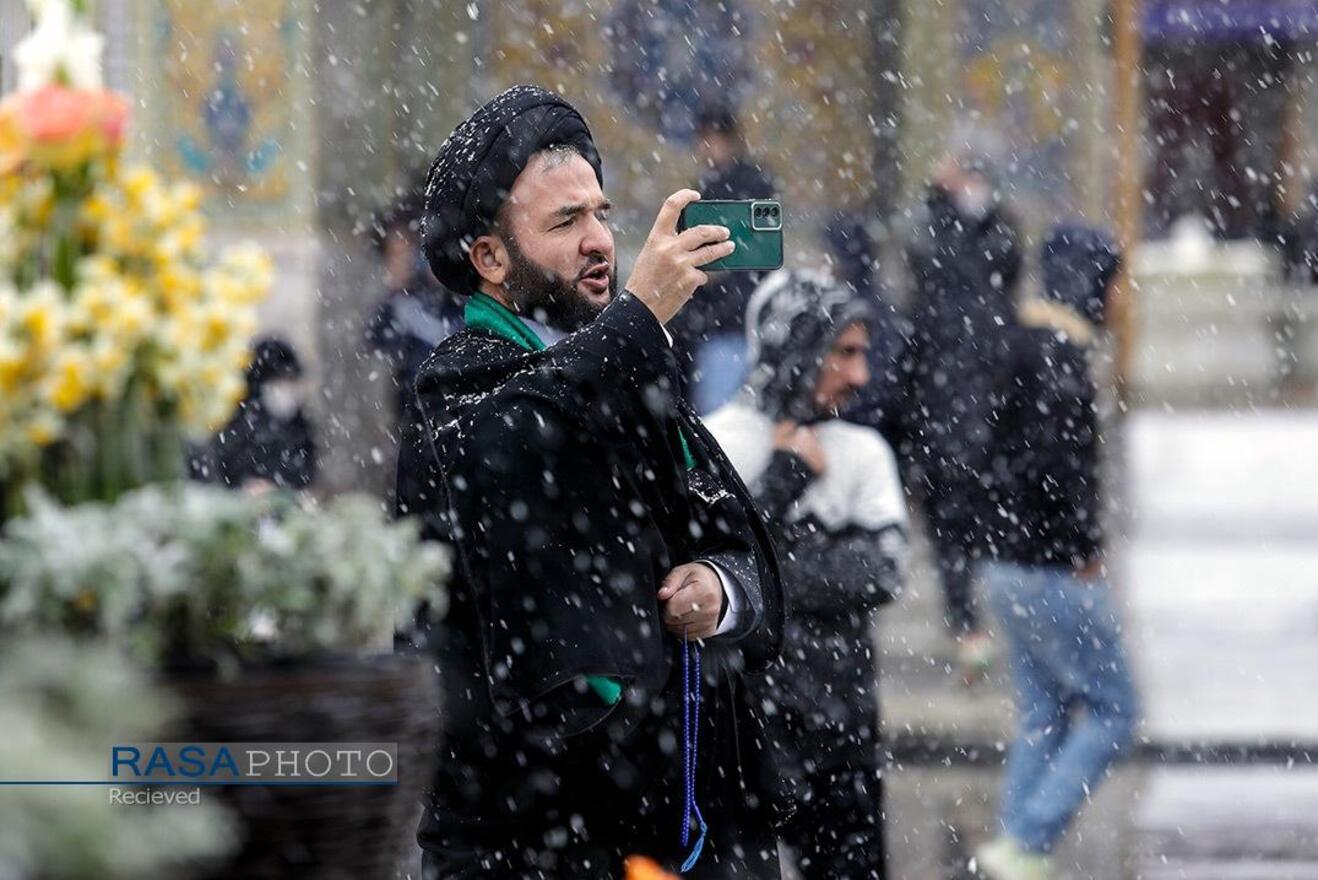 زائر حرم حضرت ثامن الحجج (علیه‌السلام) از زیبایی‌های حرم مطهر رضوی در هوای برفی عکس می‌گیرد
